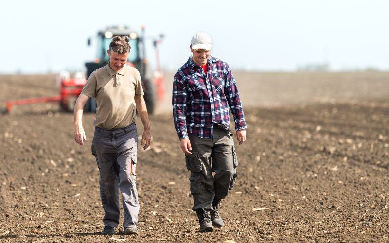 dwóch rolników na polu z pracującym traktorem w tle